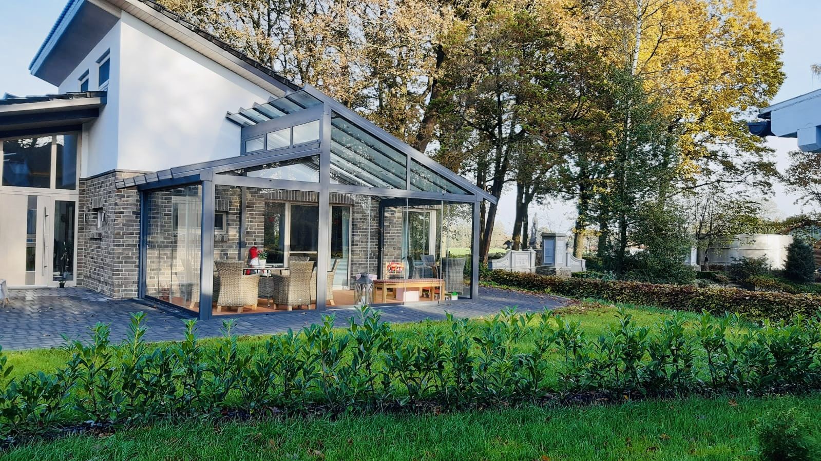 Dasselbe Haus nach der Fertigstellung: Kaltwintergarten mit Glaswänden und gepflegtem Garten