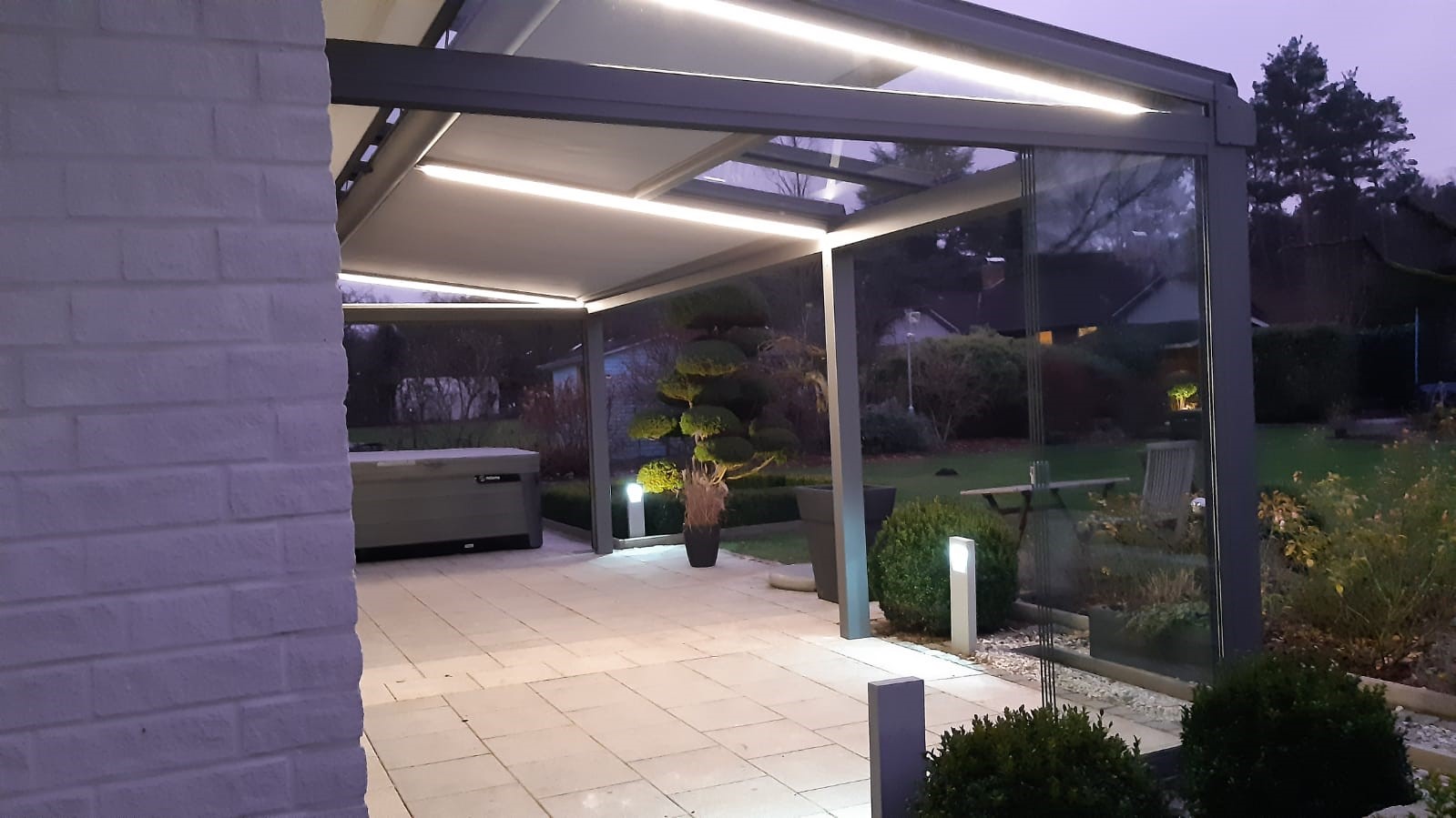 Beleuchtete Terrasse in der Abenddämmerung, geschützt durch Glasschiebewände