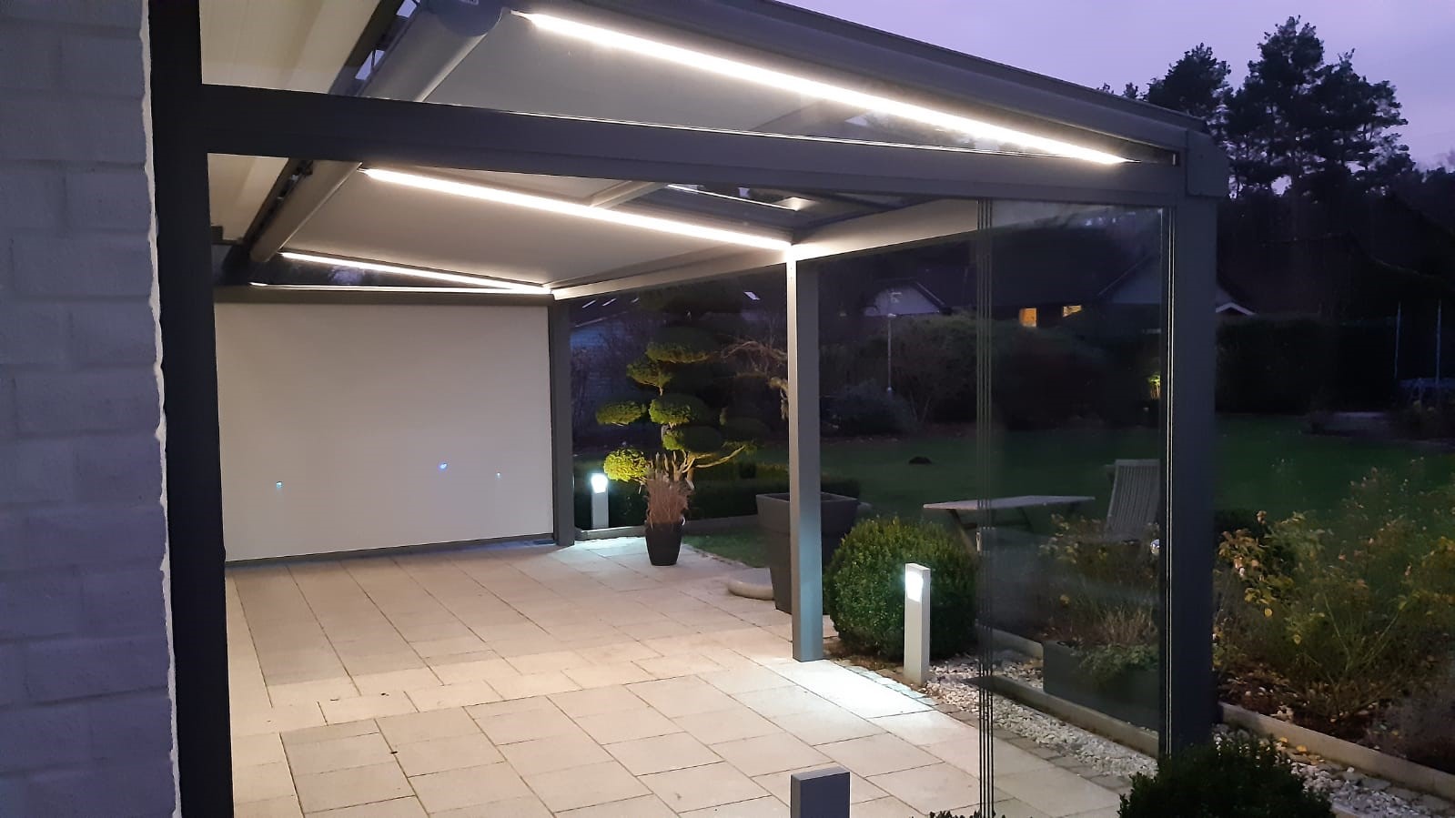 Überdachte Terrasse am Abend mit integrierter LED-Beleuchtung und Glasschiebewänden