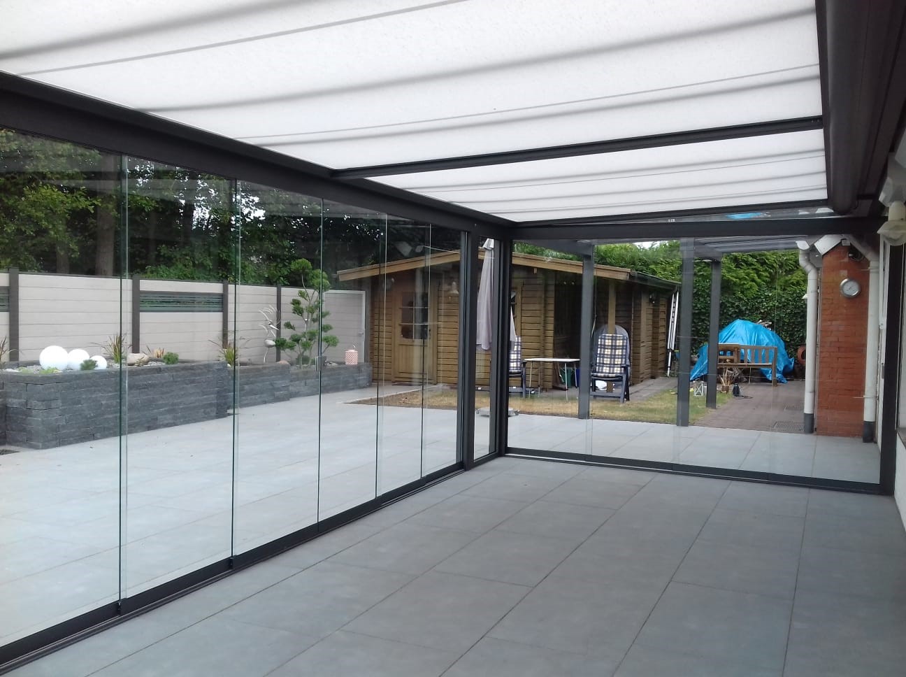 Blick von der Terrasse auf das Glasdach mit Markise und Aluminium-Profilen